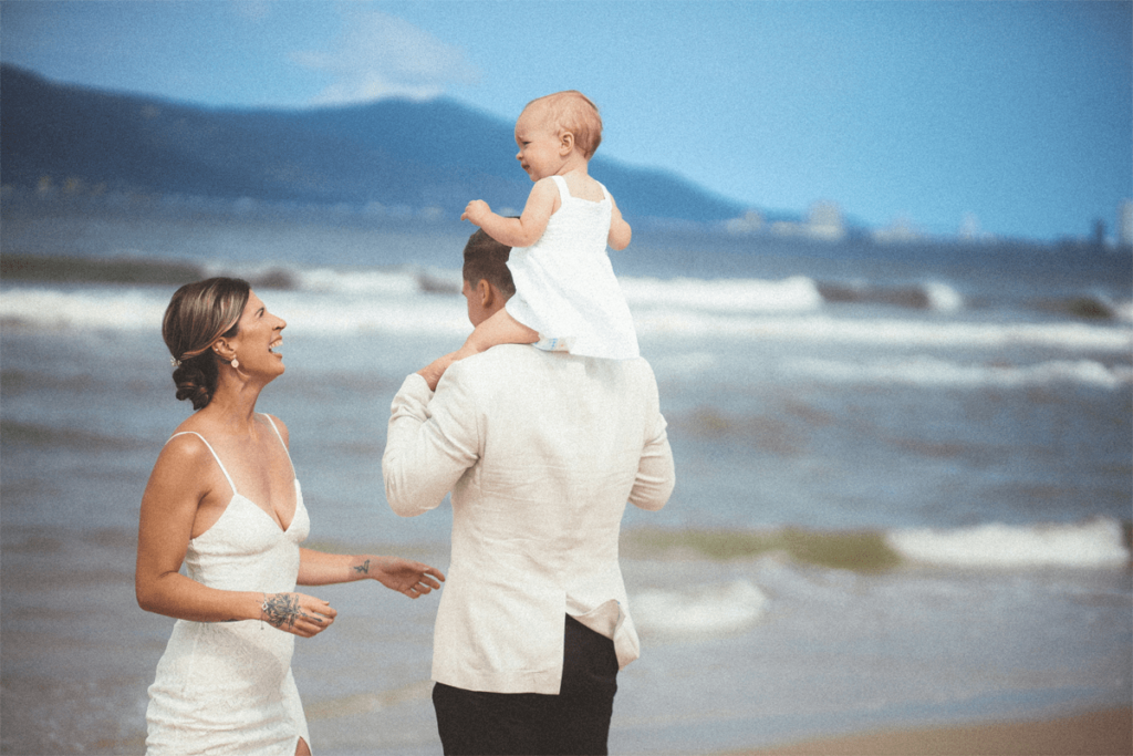 candid moment of beach wedding couple playing with baby daughter during family photo session in Brisbane