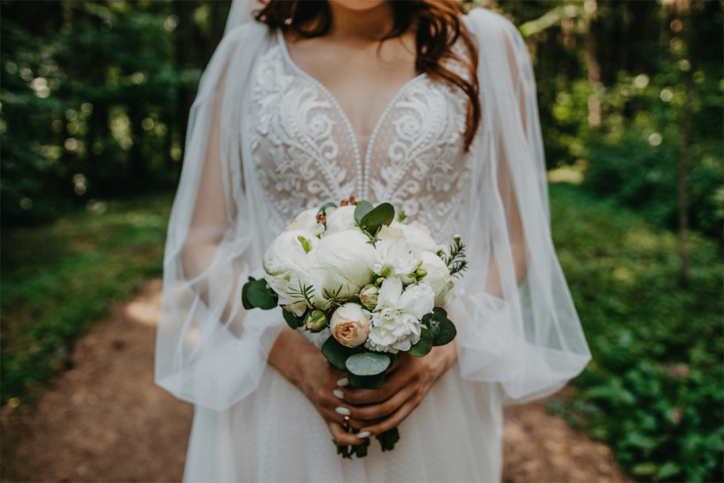 bride in lace wedding dress holding floral bouquet at outdoor forest ceremony