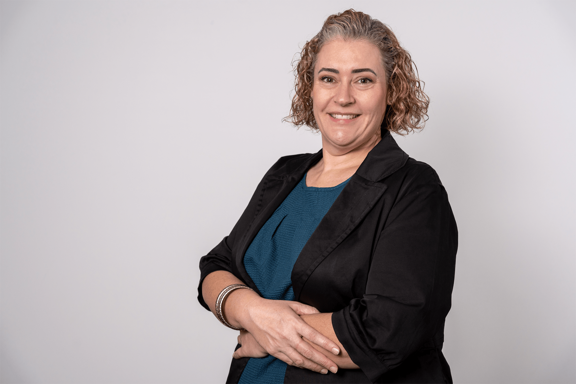 Same woman in black blazer over teal dress, arms crossed and smiling. Casual corporate portrait by Brisbane headshot photographer.